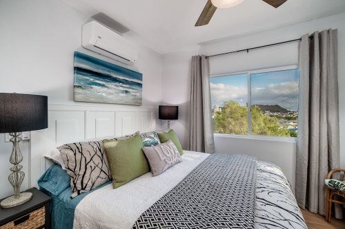 Cozy bedroom with a large bed, decorative pillows, and a view of mountains through a window. Modern decor and lighting.