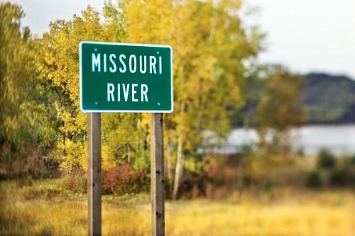 Green sign reading "Missouri River" with autumn trees and a river in the background.