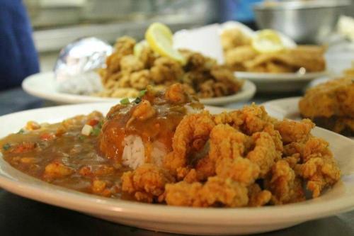 A plate of fried seafood with rice and gravy, accompanied by a side of fried food and lemon wedges in the background.