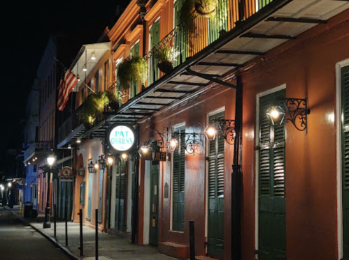 A quiet street at night featuring colorful buildings, lanterns, and a sign for Pat O'Brien's.