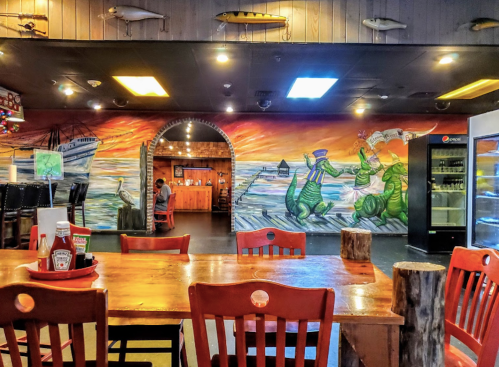 A colorful mural of sea creatures adorns a restaurant interior, with wooden tables and chairs in the foreground.
