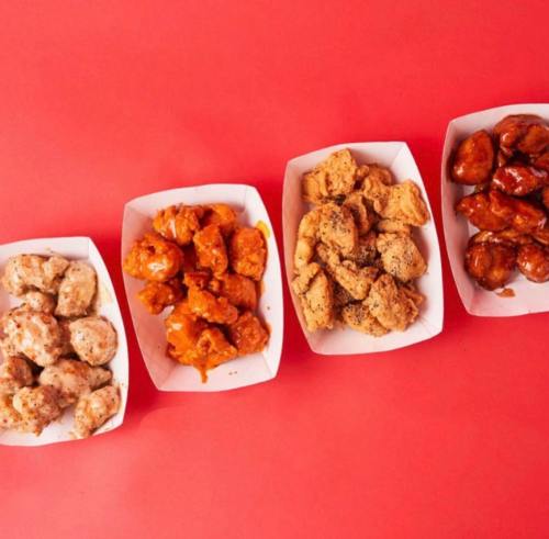 Four trays of chicken bites in various sauces on a red background.