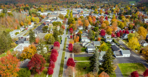 Aerial view of a small town in autumn, showcasing vibrant fall foliage in red, orange, and yellow across the landscape.