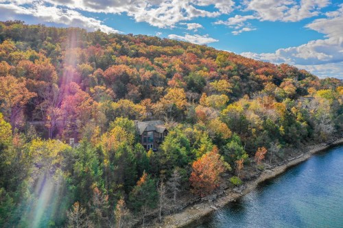 Aerial view of a lakeside house surrounded by vibrant autumn foliage and a clear blue sky.