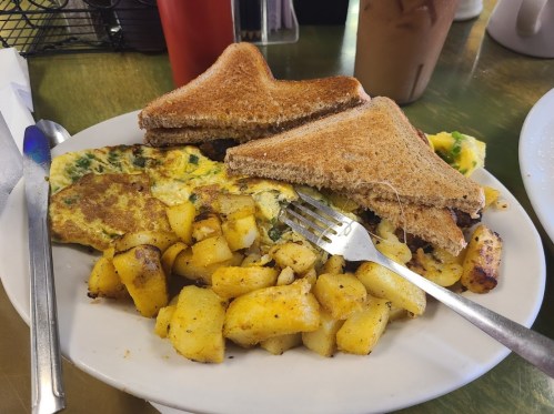 A plate with an omelette, golden potatoes, and two slices of toasted bread, with a fork resting on the side.