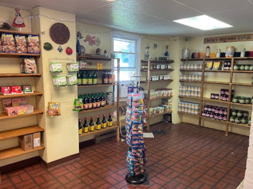 Interior of a small store with shelves of snacks, drinks, and various goods, featuring a display rack in the center.