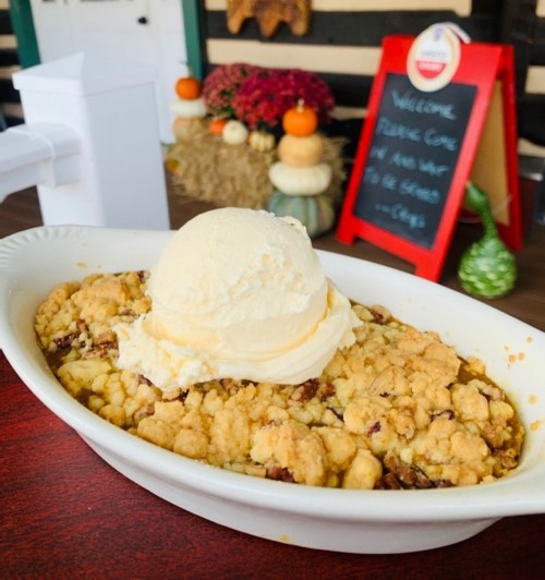 A warm dessert with a crumbly topping and a scoop of vanilla ice cream, set against a cozy autumn backdrop.