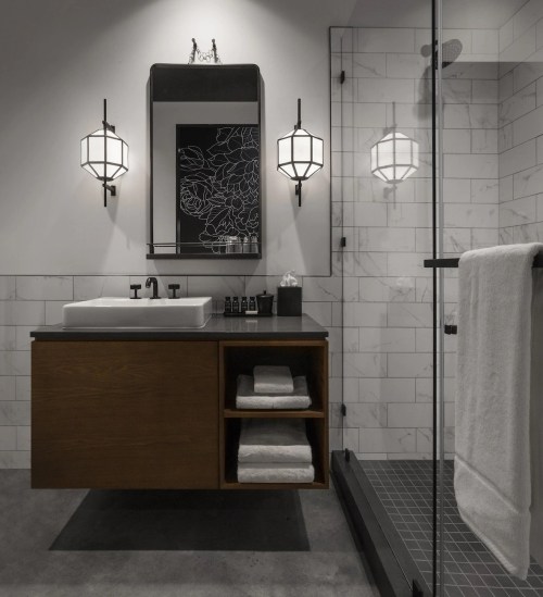 Modern bathroom featuring a sleek sink, wooden vanity, glass shower, and stylish wall sconces.
