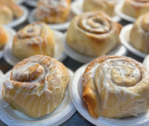 Freshly baked cinnamon rolls drizzled with icing, arranged on white plates.