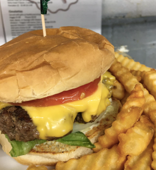 A cheeseburger with lettuce, tomato, and melted cheese, served with crinkle-cut fries on the side.