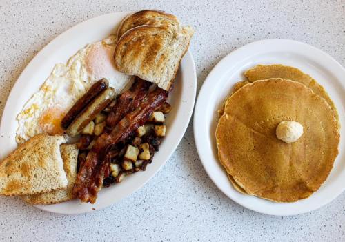 A plate of breakfast featuring eggs, bacon, sausage, toast, potatoes, and a side of pancakes with butter.