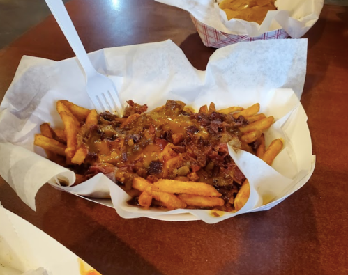 A serving of loaded fries topped with cheese and bits of meat, served in a paper-lined basket.