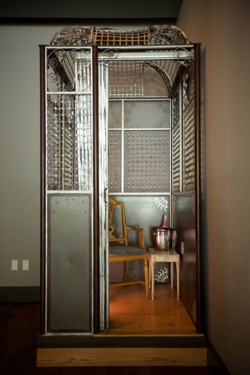 A vintage-style elevator with ornate metalwork, featuring a chair and a small table with a champagne bucket inside.