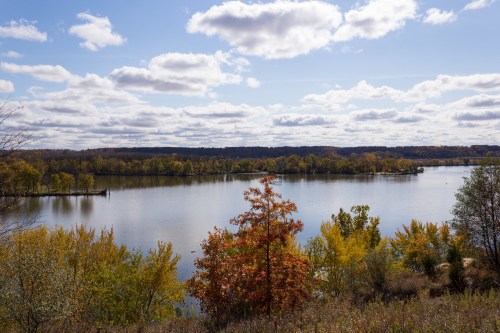 A serene lake surrounded by autumn foliage under a partly cloudy sky.