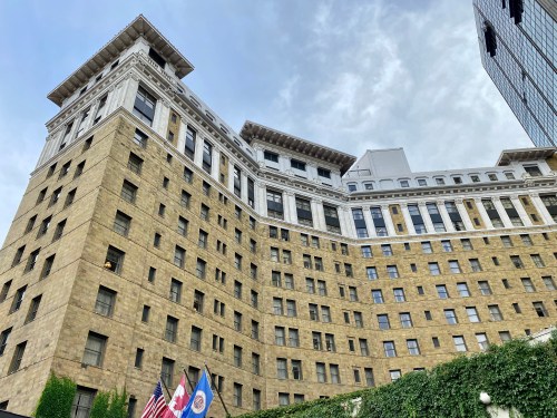 Historic building with a stone facade, multiple stories, and flags in front, under a cloudy sky.