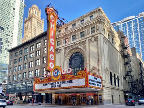 The Chicago theater marquee displays "Bond: Stories of Surrender" with "Sold Out" beneath, surrounded by city buildings.