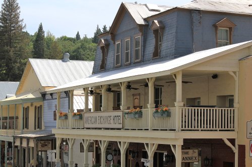Historic buildings with balconies and flower boxes in a quaint town setting, surrounded by trees and hills.