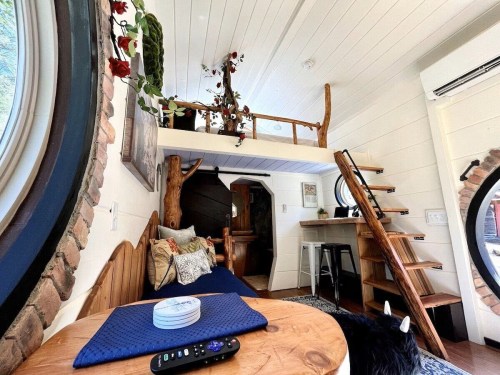 Cozy interior of a tiny home featuring a loft, wooden accents, and a circular window.