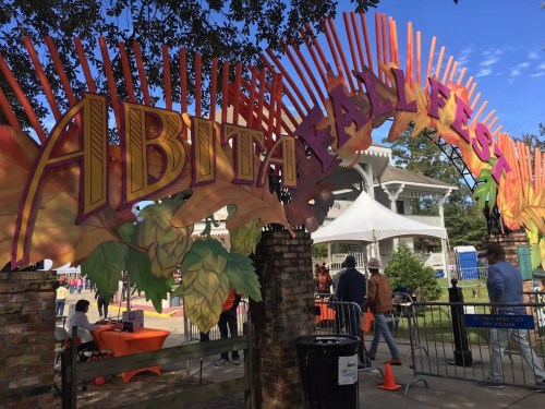 Colorful entrance archway for the Abita Fall Fest, with people and tents in the background under a clear blue sky.