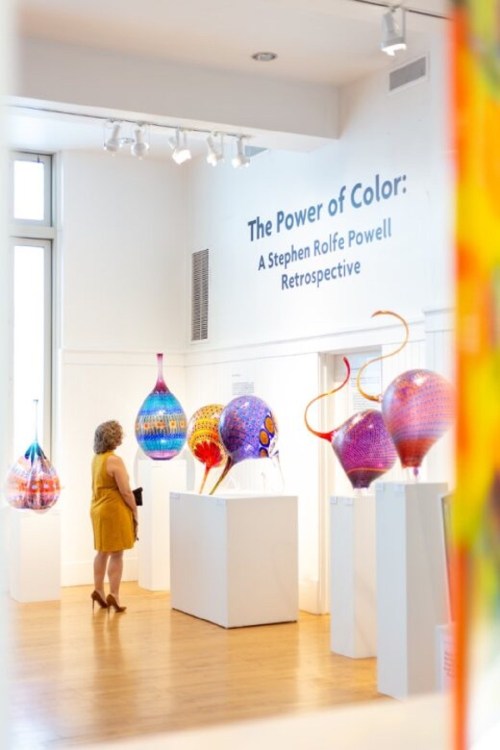 A visitor admires colorful glass sculptures at "The Power of Color: A Stephen Rolfe Powell Retrospective" exhibition.