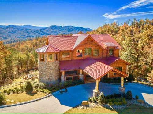 A large, rustic mountain home with a red roof, surrounded by colorful autumn trees and scenic mountains in the background.