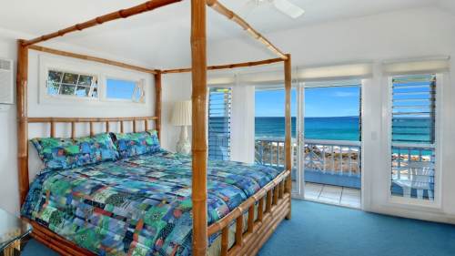Bright bedroom with a four-poster bed, colorful bedding, and ocean views through large windows.