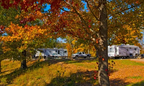 Two RVs parked among vibrant autumn trees with colorful leaves, set in a serene outdoor landscape.