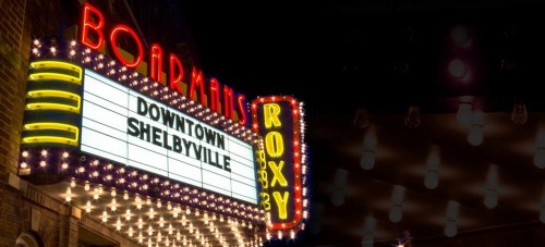 Neon marquee of Boardman's Roxy theater in downtown Shelbyville, illuminated with bright lights at night.