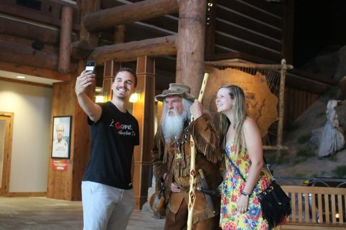 A man and a woman pose for a selfie with an older man in a costume, inside a rustic building.