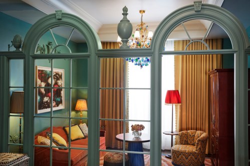 A stylish room with arched windows, colorful curtains, a chandelier, and cozy furniture, creating a warm atmosphere.