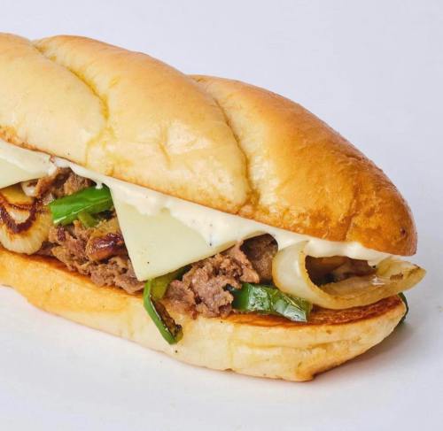 A delicious sandwich with tender beef, grilled onions, green peppers, and creamy sauce on a soft hoagie roll.