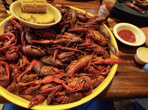 A large yellow platter filled with cooked crawfish, corn, and dipping sauces on a wooden table.