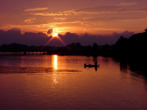A serene sunset over a lake, with vibrant orange and purple hues reflecting on the water and a small boat in the foreground.