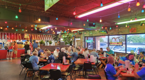 A lively restaurant scene with colorful lights, diners enjoying meals at tables, and a vibrant atmosphere.