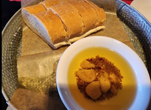 A plate with sliced bread next to a bowl of olive oil and garlic dip, served on parchment paper.