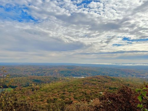 A panoramic view of rolling hills covered in autumn foliage under a cloudy sky.
