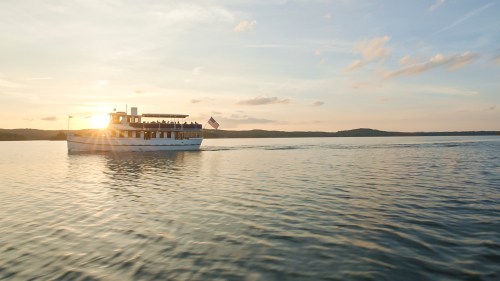 A boat sails on calm waters at sunset, with a scenic landscape in the background.