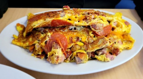 A large, loaded omelette filled with meats and cheese, served on a white plate.