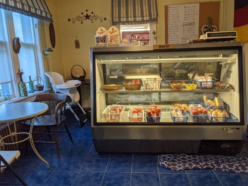 A display case filled with various meats and produce, next to a small dining table and high chair in a cozy kitchen.