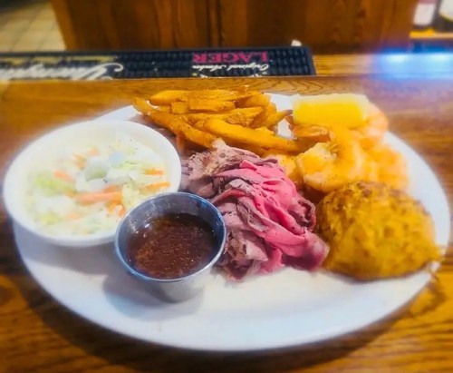 A plate of food featuring sliced roast beef, sweet potato fries, coleslaw, a biscuit, and a small cup of sauce.