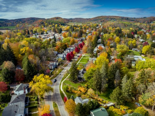 Aerial view of a colorful autumn landscape with trees in vibrant hues and a winding road through a quaint neighborhood.