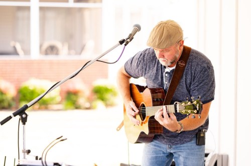 A musician playing an acoustic guitar on stage, wearing a cap and focused on his performance.
