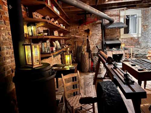 A cozy workshop with wooden shelves, lanterns, tools, and rustic decor, illuminated by warm light.
