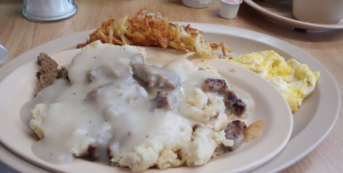 A plate of biscuits and gravy, hash browns, and an omelet on a wooden table.