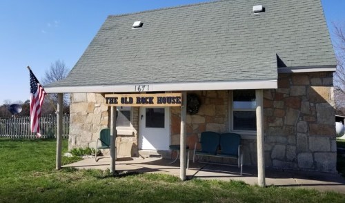 A stone house with a sloped roof, featuring a sign that reads "The Old Rock House" and an American flag.