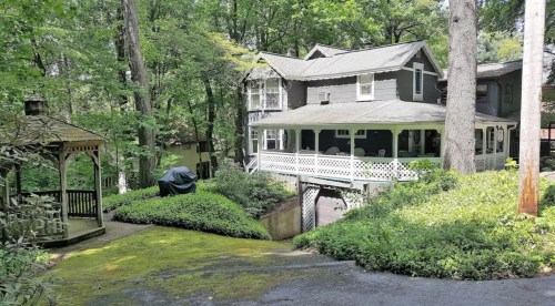 A charming gray house surrounded by trees, with a gazebo and lush greenery in the foreground.