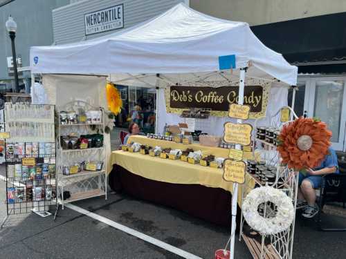 A market stall with a white canopy displaying coffee candy products, jars, and decorative items.