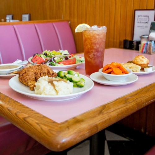 A table with a variety of dishes: fried chicken, mashed potatoes, salad, and a drink, all served in a diner setting.