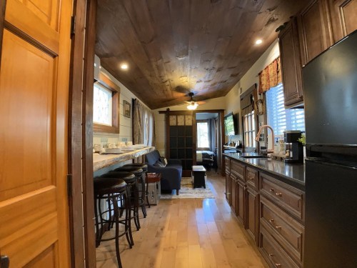 Cozy kitchen and living area with wooden ceiling, bar seating, and modern appliances in a warm, inviting space.