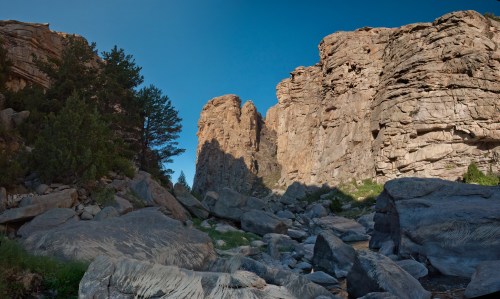 A rocky canyon with towering cliffs and scattered boulders under a clear blue sky.